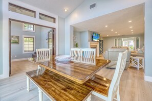 A spacious dining area with a wooden table and white chairs, a fireplace, and a television in the background. - IslandTime Vacation! (Indian Rocks Beach)
