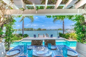 Un espace aménagé au bord de la piscine, avec vue sur l’eau, une table avec des chaises et un coin salon abrité.