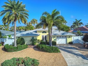 A yellow house with a white garage, surrounded by palm trees and well-maintained landscaping. - IslandTime Vacation! (Indian Rocks Beach)