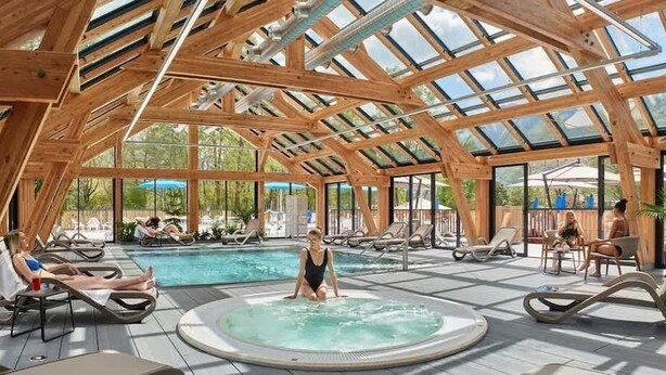 Une terrasse en bois avec un toit en verre, un jacuzzi et des chaises longues.