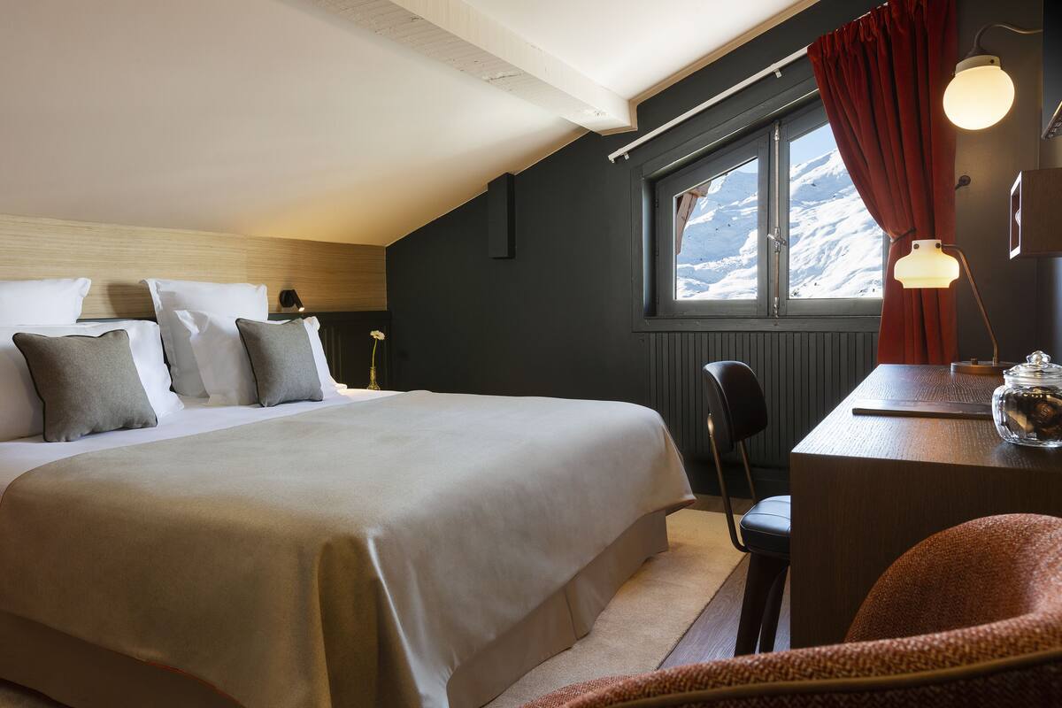 Ein Schlafzimmer mit einem großen Bett, einem Schreibtisch mit Lampe und einem Fenster mit Blick auf einen verschneiten Berg.