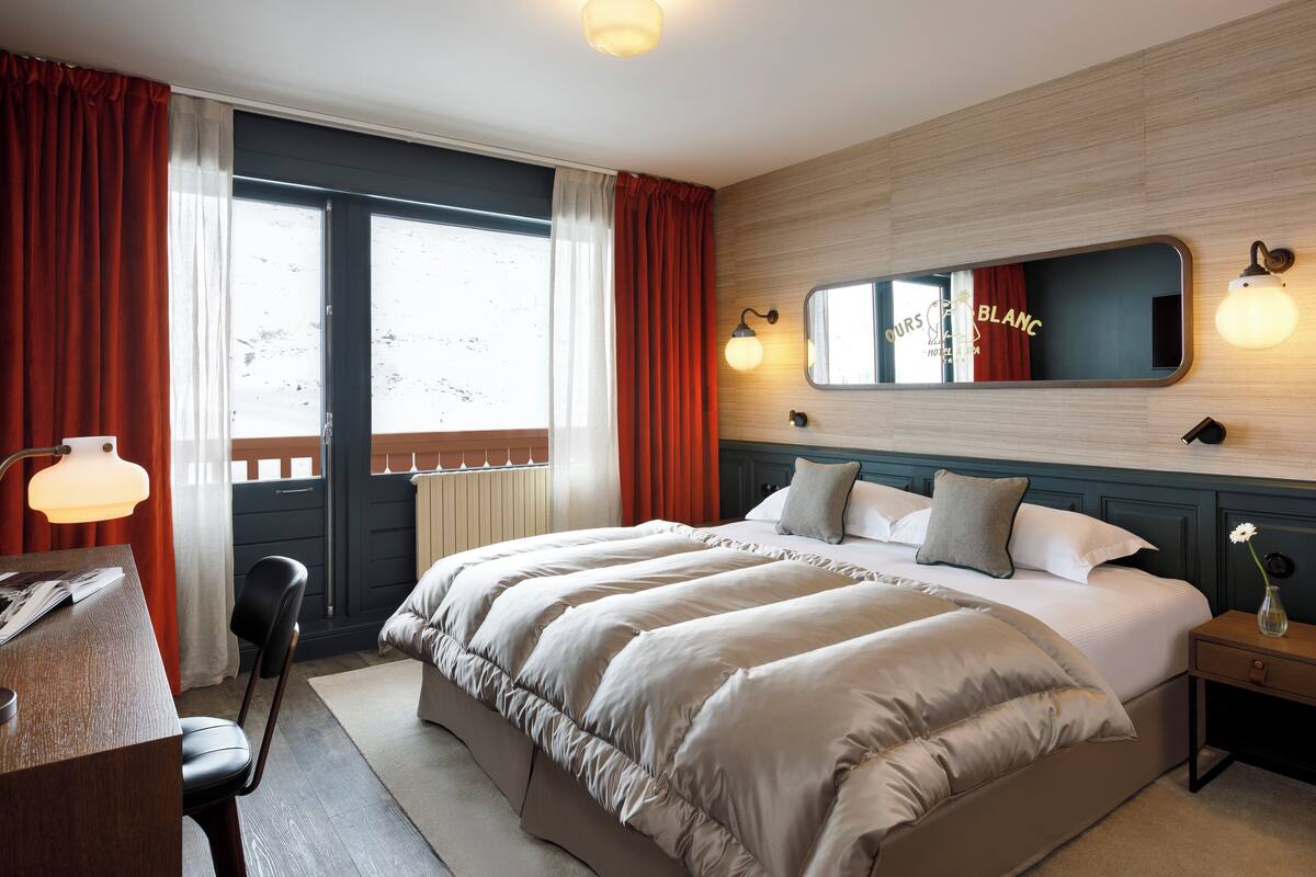 Ein Hotelzimmer mit einem großen Bett, einem Schreibtisch mit Lampe, einem Sessel und einem Nachttisch mit einer Vase.