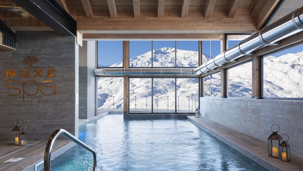 Un spa con vistas a montañas nevadas, una piscina y un techo de madera.