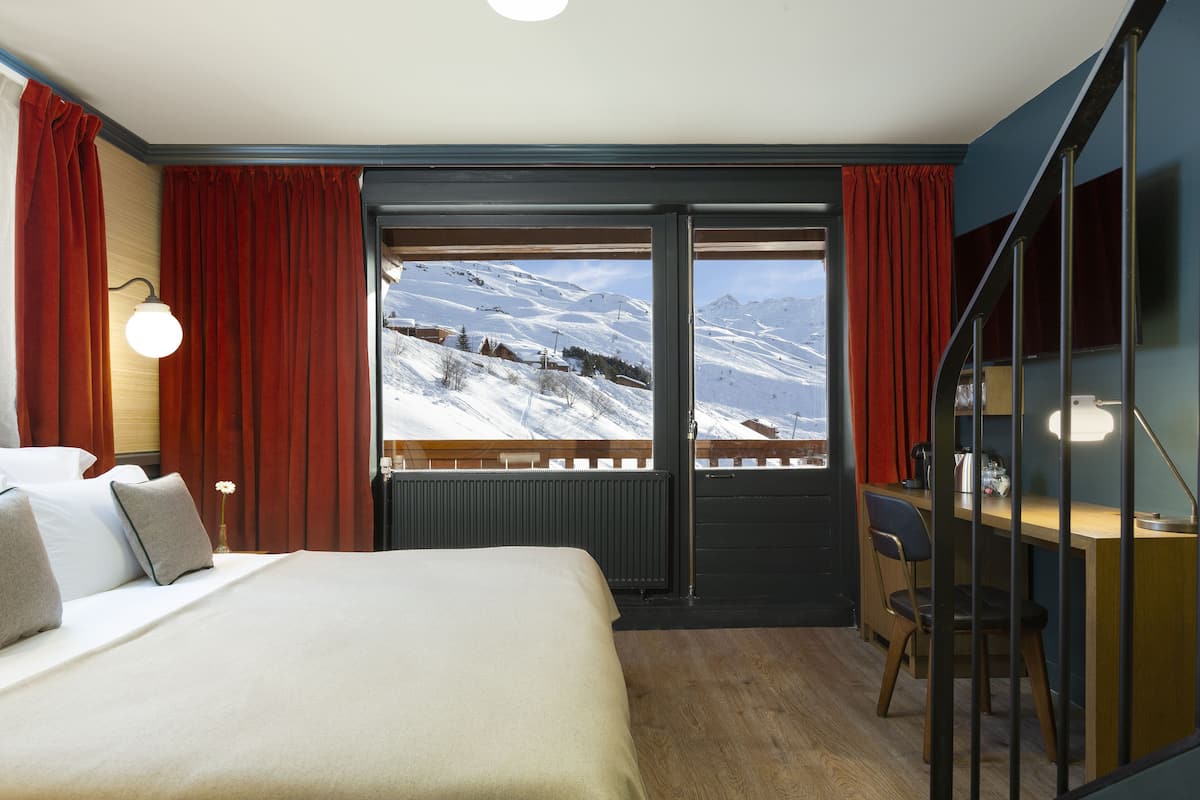 Ein Hotelzimmer mit einem großen Bett, einem Schreibtisch und Blick auf verschneite Berge.