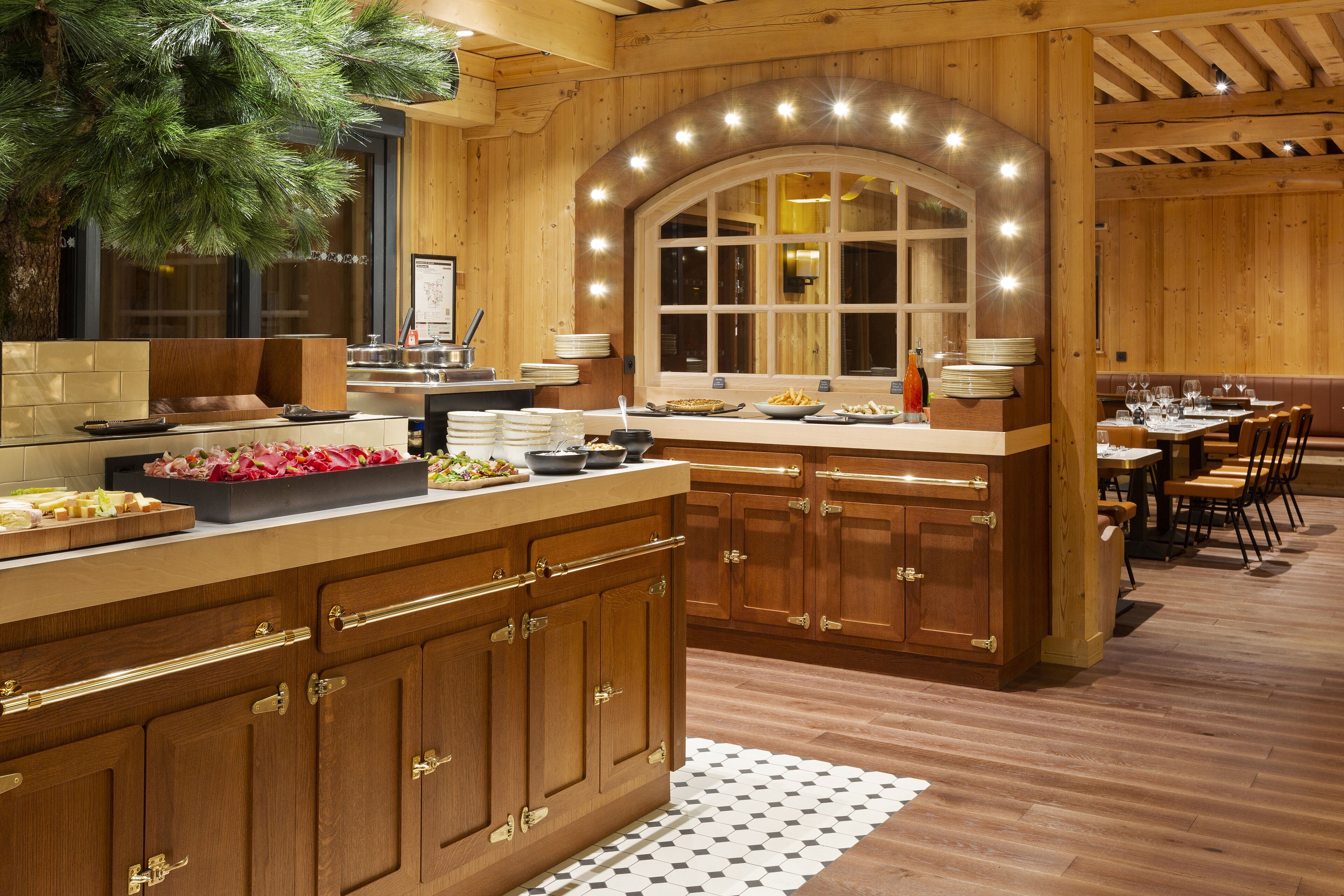 A wooden interior with a central island, dining area, and a large window with lights.