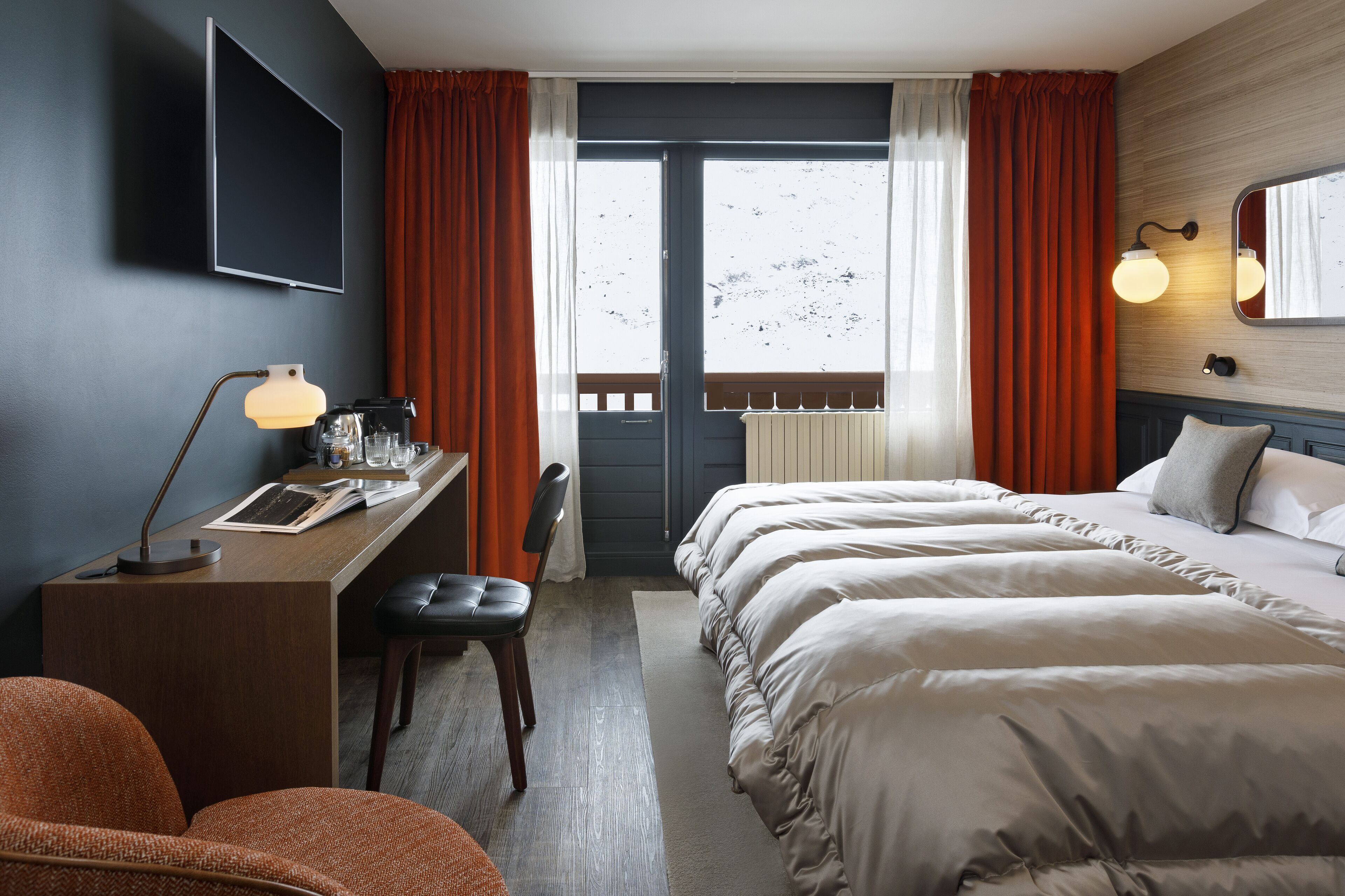 A hotel room with a bed, desk, chair, and a view of the outdoors.