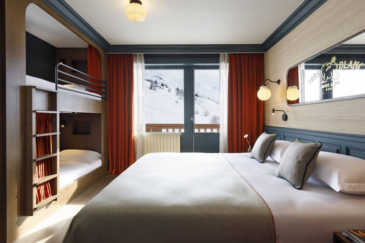 Ein Hotelzimmer mit Etagenbett, einem großen Bett, einem Fenster mit Blick auf eine verschneite Landschaft und einem Spiegel mit einem Schild darüber.