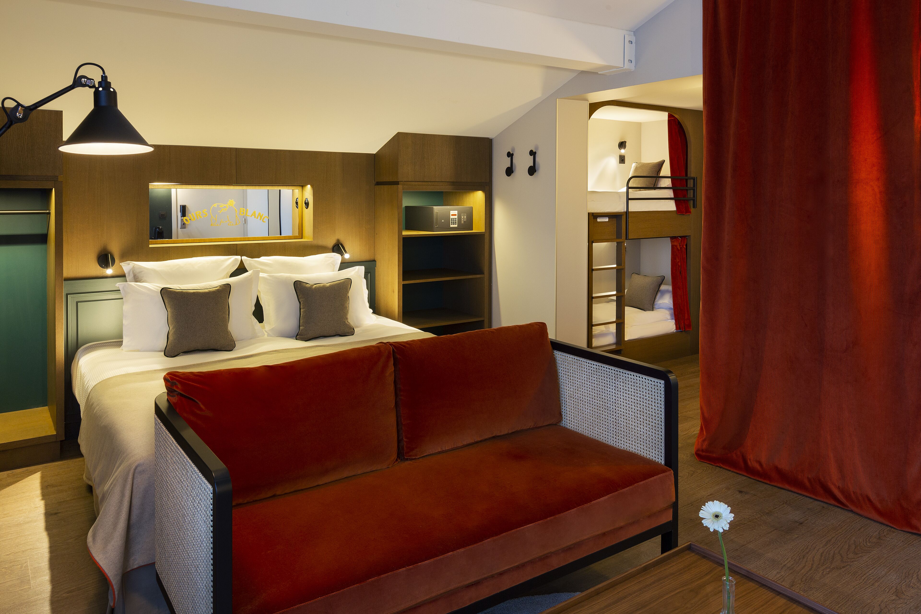 A modern hotel room with a bed, a red sofa, a desk, and a bunk bed.