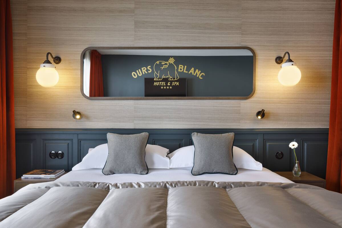 Ein Hotelzimmer mit einem Bett, Kissen, einem Nachttisch, einem Spiegel und Wandleuchten.