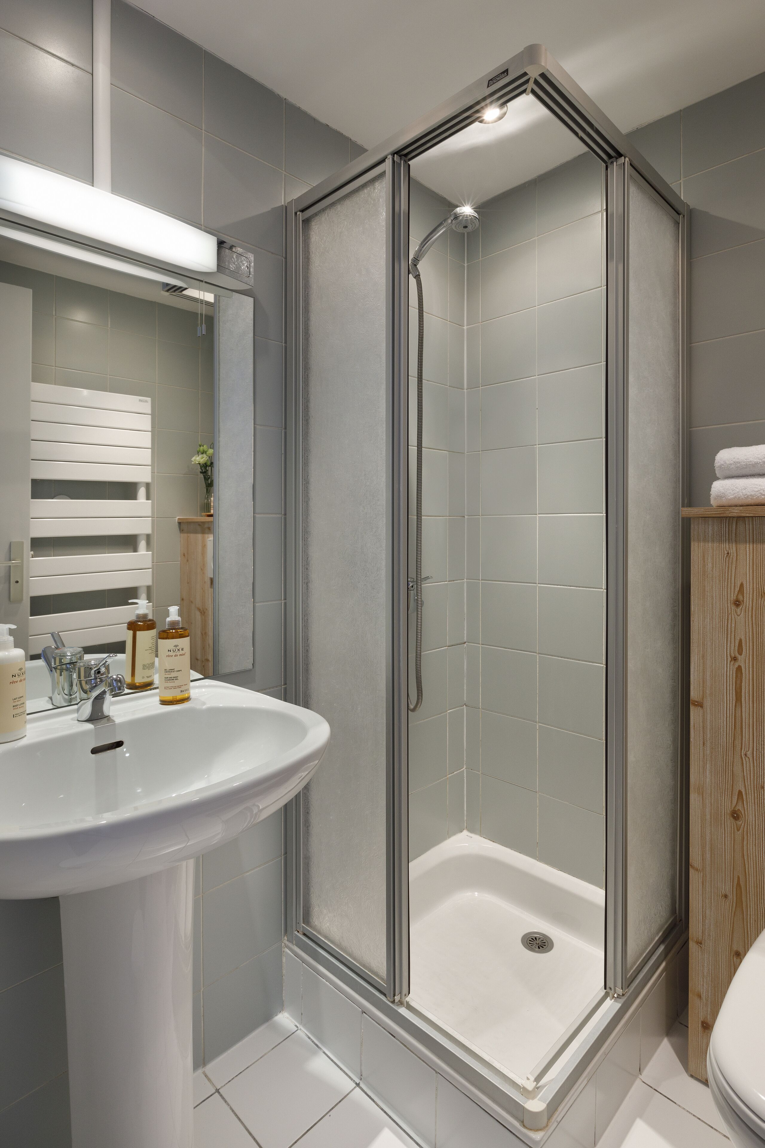Een moderne badkamer met een douchecabine van glas, een wit wastafelmeubel en een houten kast.