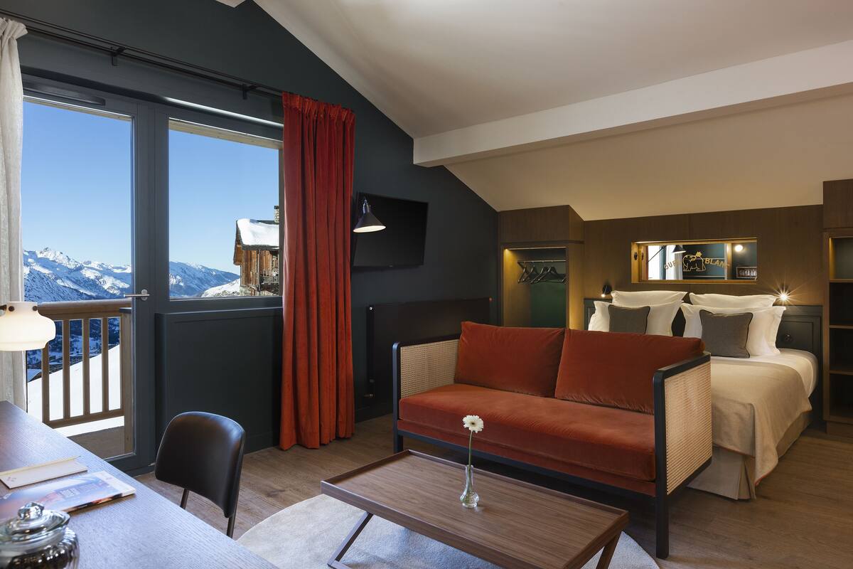 Ein modernes Hotelzimmer mit einer Couch, einem Esstisch, einem Couchtisch und Blick auf schneebedeckte Berge.