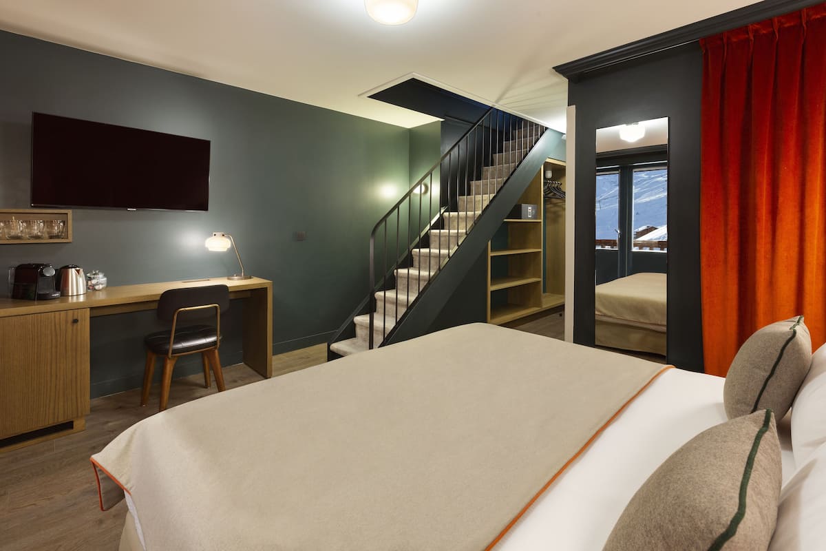 Ein Schlafzimmer mit Bett, Schreibtisch, Stuhl und einer Treppe, die auf einen Balkon führt.