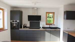 Eine moderne Küche mit dunklen Schränken, einem eingebauten Backofen und einem Fenster, das für natürliches Licht sorgt.