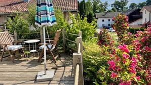 Eine Holzterrasse mit Gartenmöbeln, einem gestreiften Sonnenschirm und einem Garten mit rosa Blumen.