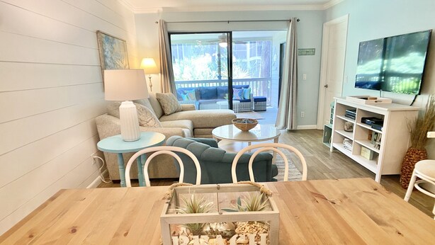 Uma sala de estar moderna com uma mesa de jantar de madeira, sofá, televisão e uma varanda com vista.