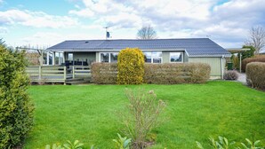 Ein eingeschossiges Haus mit umzäunter Terrasse, gepflegtem Rasen und verschiedenen Sträuchern und Pflanzen.