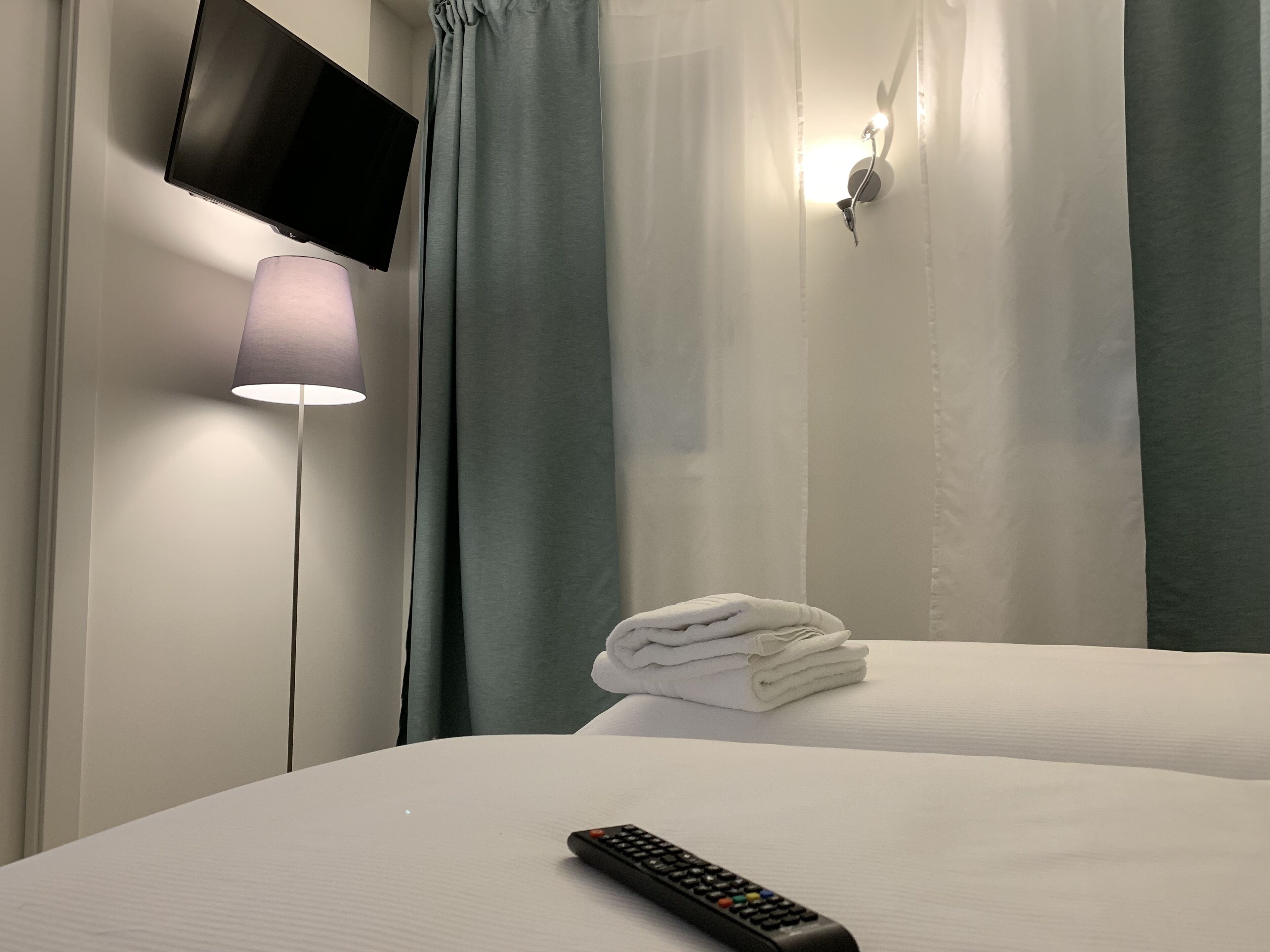 Una cama bien hecha con un control remoto, una lámpara y un televisor montado en la pared.