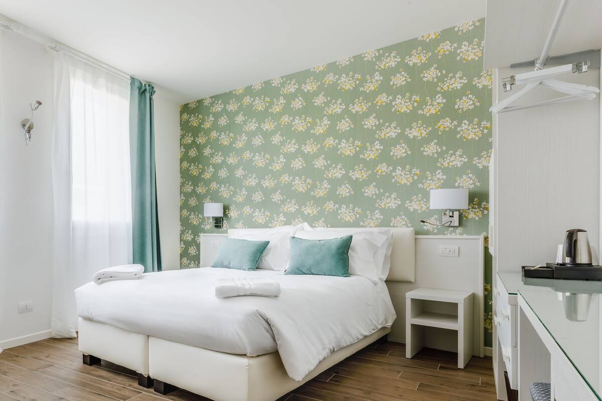 Habitación de hotel con cama, mesitas de noche, escritorio y zona de ducha.