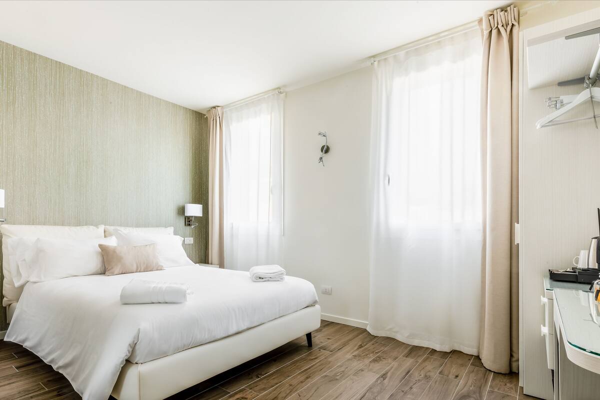 Una habitación de hotel con cama, mesitas de noche, un espejo y un armario.