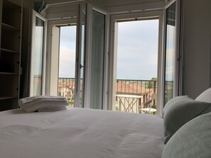 A bedroom with a large bed, a view of a balcony, and a window with curtains. - Casa Baci (Lazise)