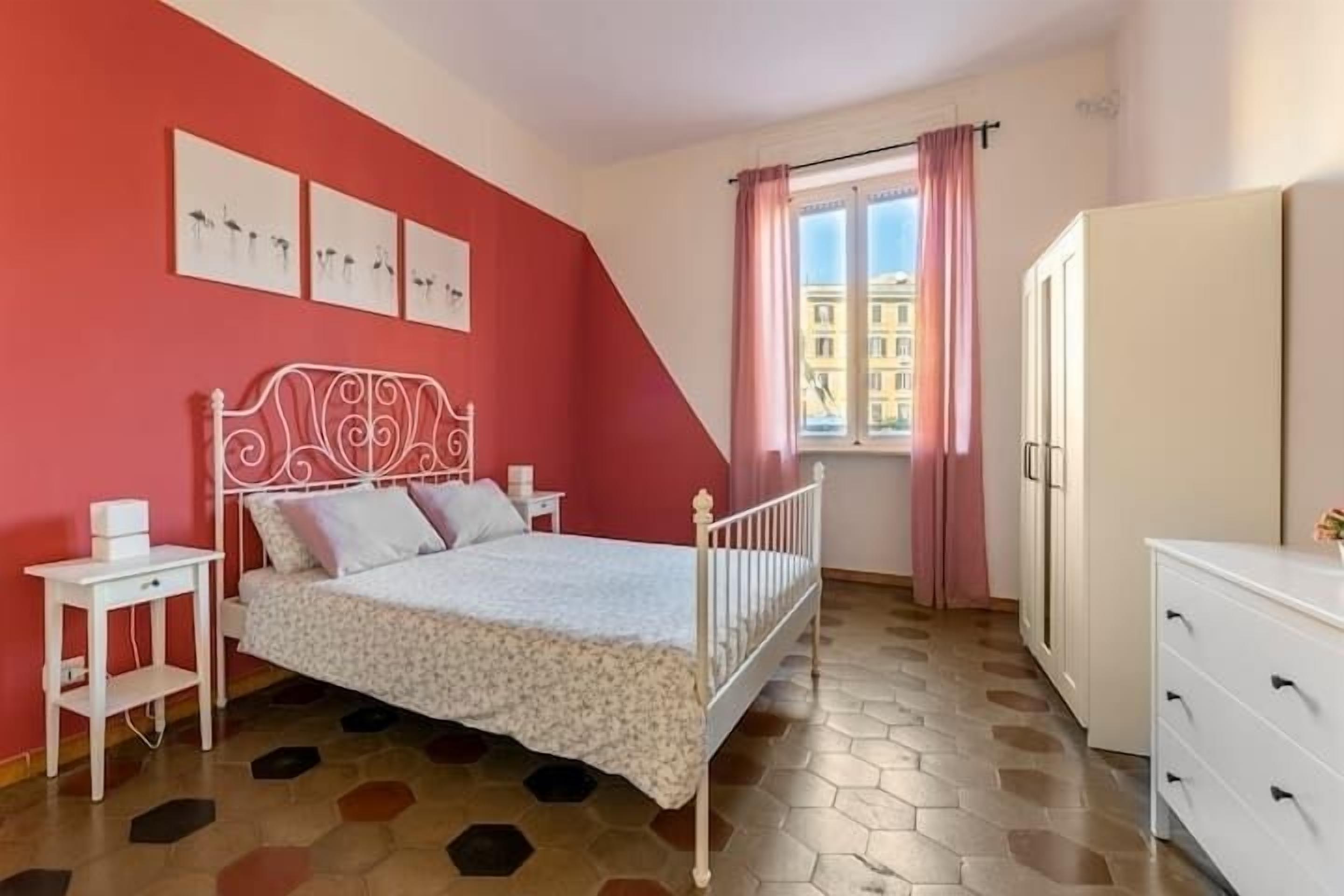 A bedroom with a white metal bed frame, a white dresser, and a window with pink curtains.