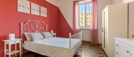 A bedroom with a white metal bed frame, a white dresser, and a window with pink curtains.