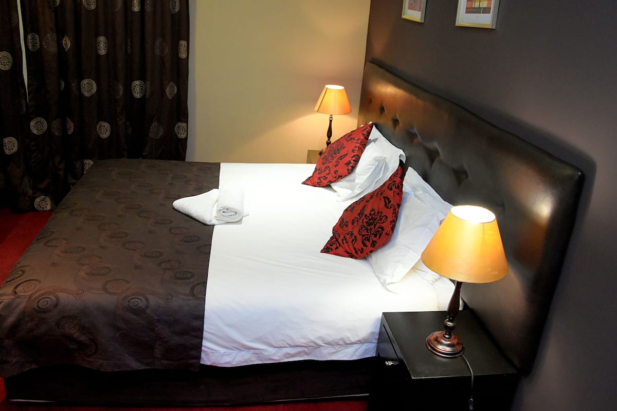 A neatly made bed with white and red pillows, two bedside lamps, and a dark headboard.