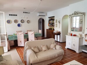 A living room with a beige sofa, dining table with chairs, a bookshelf, a white cabinet, and a large mirror. - Villa with jetty on Magra river (Ameglia, La Spezia - Liguria)