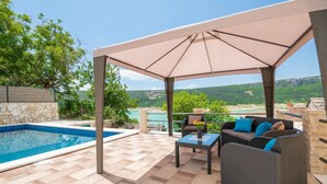 A covered outdoor area with a pool, seating, and a scenic view.