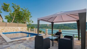 An outdoor patio with a pool, wicker furniture, and a view of a lake and hills.