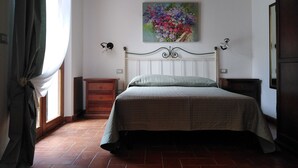 Un dormitorio con cama, mesita de noche, cómoda, un cuadro y una ventana con cortinas.