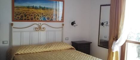 Un dormitorio con cama, un cuadro en la pared, una mesita de noche y una ventana con cortinas.