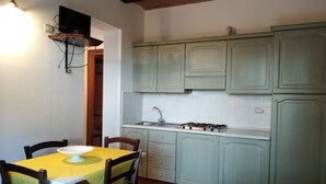 Una cocina con alacenas verde claro, una estufa a gas y un lavamanos. Hay una mesa de comedor con sillas y un mantel amarillo.