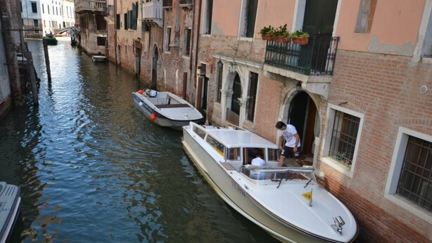 Un canal estrecho con barcos amarrados a lo largo de sus orillas, flanqueado por edificios históricos con ventanas arqueadas y balcones.