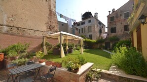 Un patio con un área de estar cubierta, plantas en macetas y un muro de ladrillo.