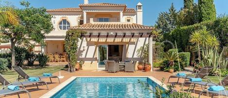 A poolside area with a pool, lounge chairs, and a patio with outdoor furniture.