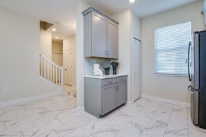 Kitchen features a grey cabinetry system, black refrigerator, and a window with blinds.