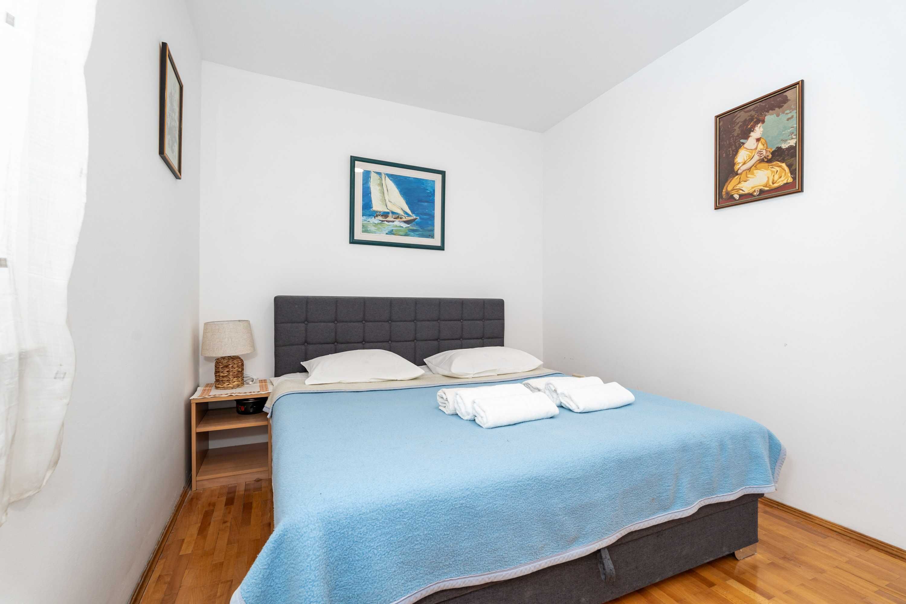 Un dormitorio con cama, mesita de noche, lámpara y dos cuadros en la pared.