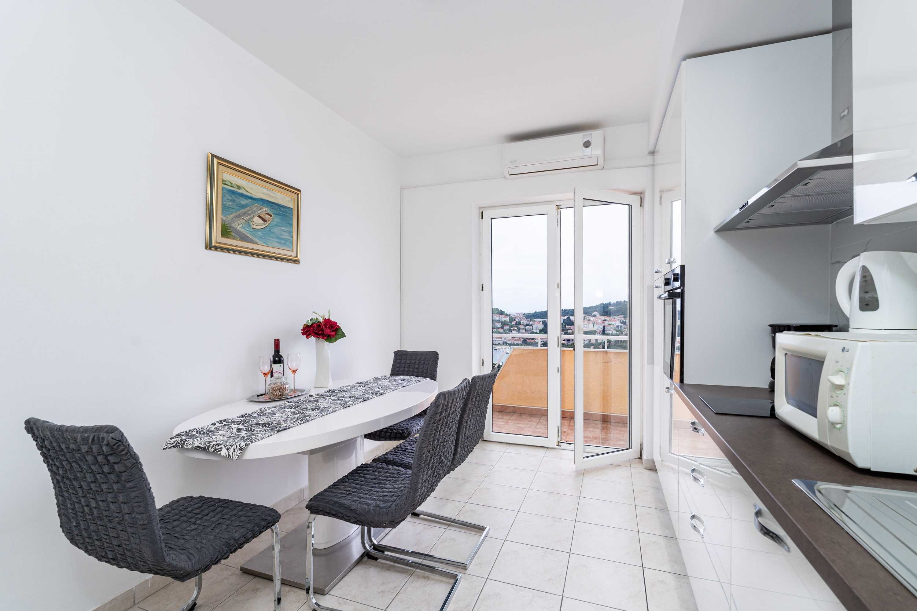 Una cocina moderna con un microondas blanco, una zona de comedor con mesa y sillas, y vistas de la ciudad a través de la puerta corredera de vidrio.