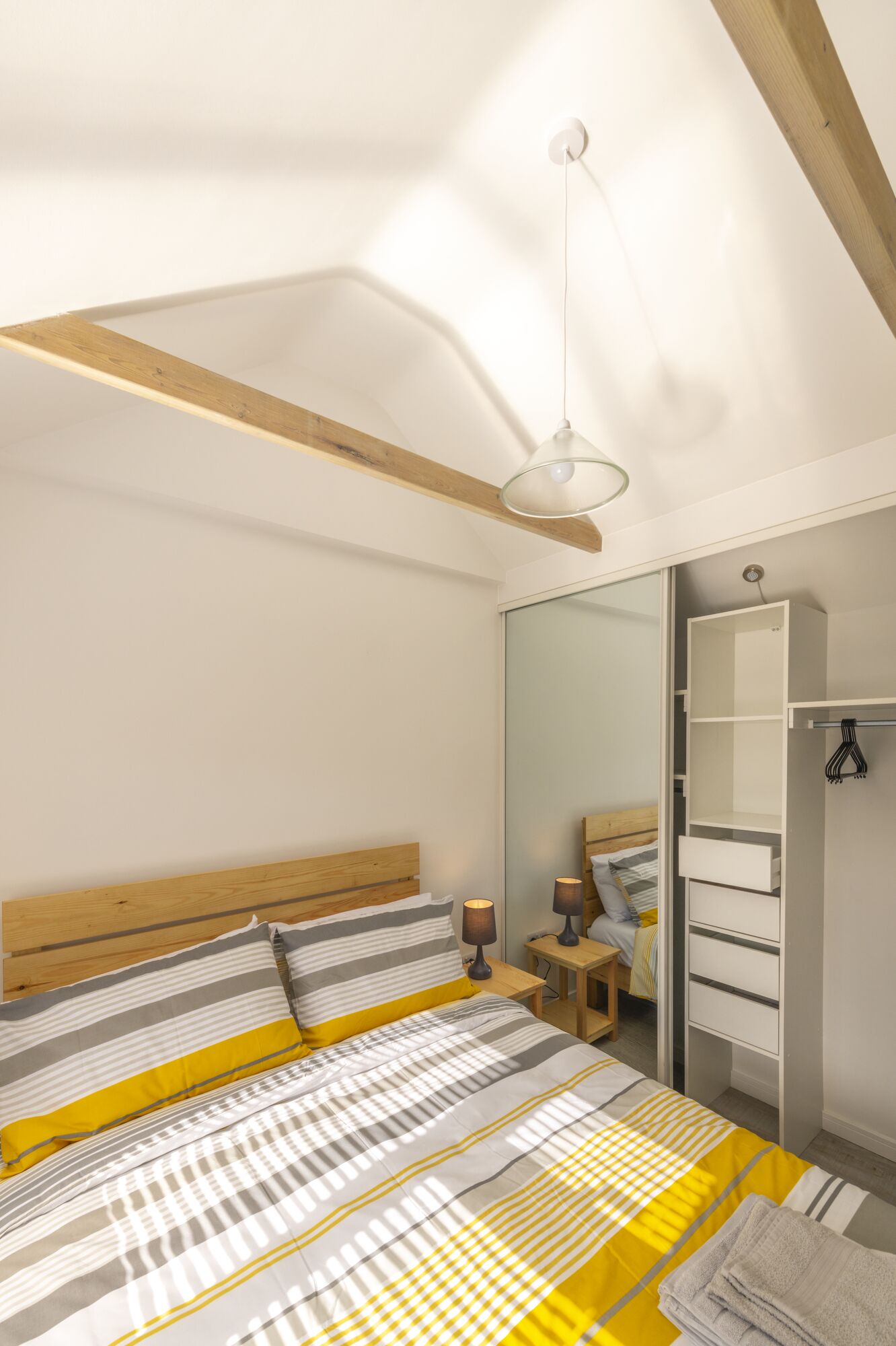 Een slaapkamer met een bed, nachtkastje, lamp, kast en spiegel.