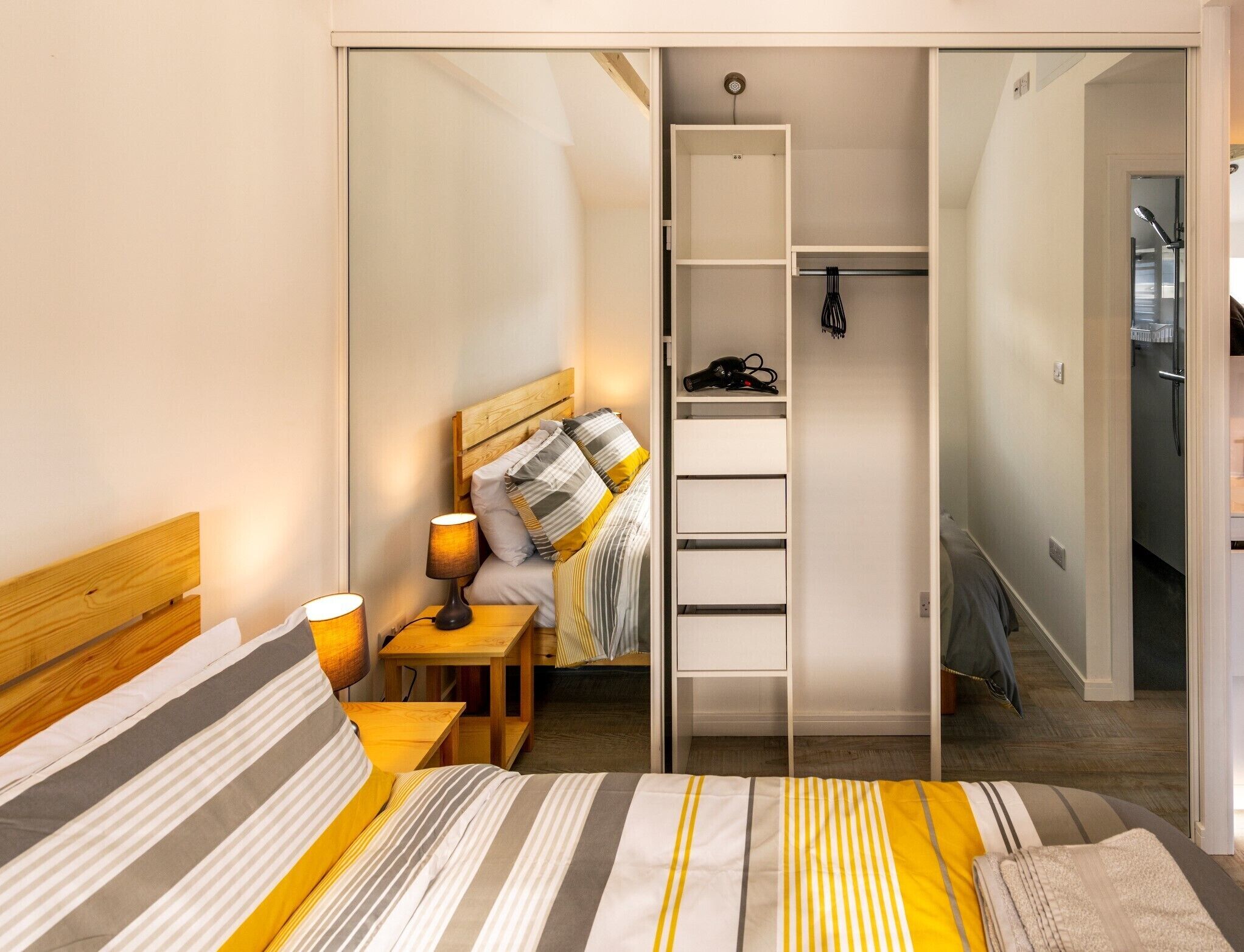 Un dormitorio con cama, mesitas de noche, lámpara, armario y un baño a la vista a través de una puerta abierta.