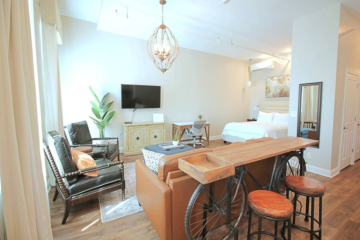 A modern hotel room with a wooden dining table, a bicycle, a sofa, and a TV.