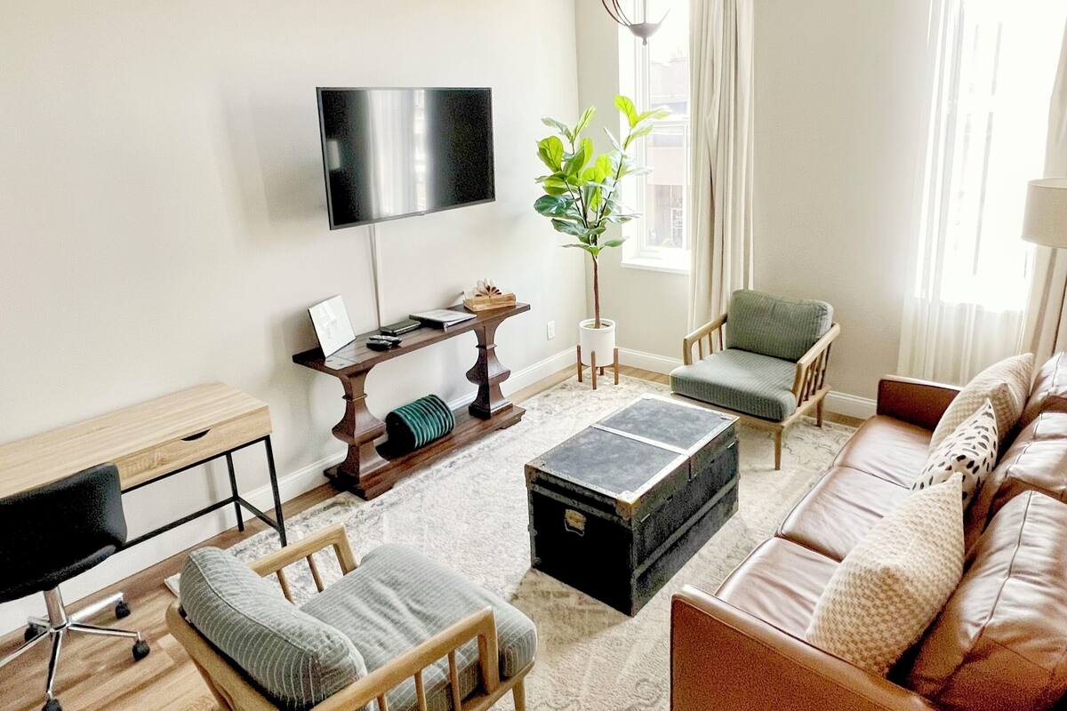A modern living room with a flat-screen TV, a wooden desk, a comfortable sofa, and a coffee table.