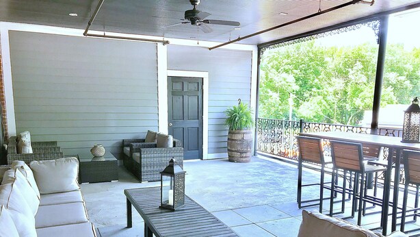 Un patio techado con mobiliario exterior, ventilador de techo y vista a la vegetación.