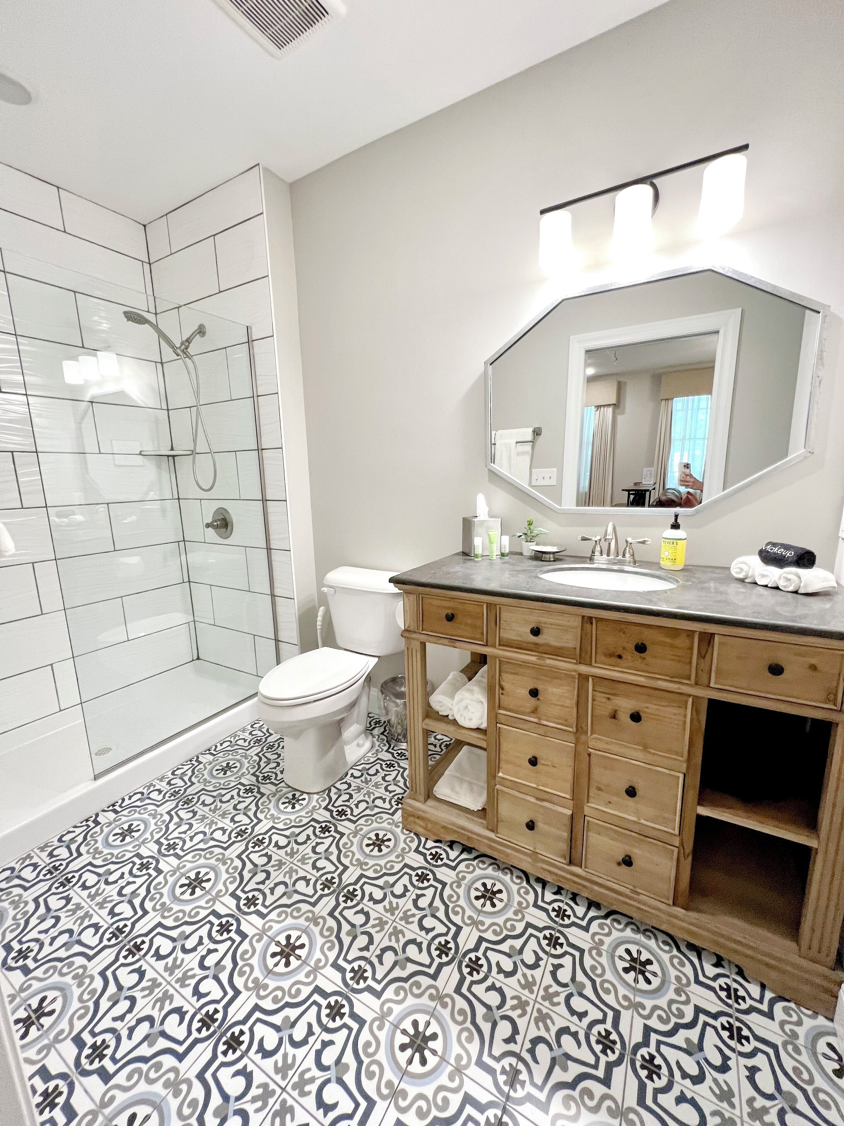Baño con ducha, inodoro, tocador y baldosas de suelo estampadas.