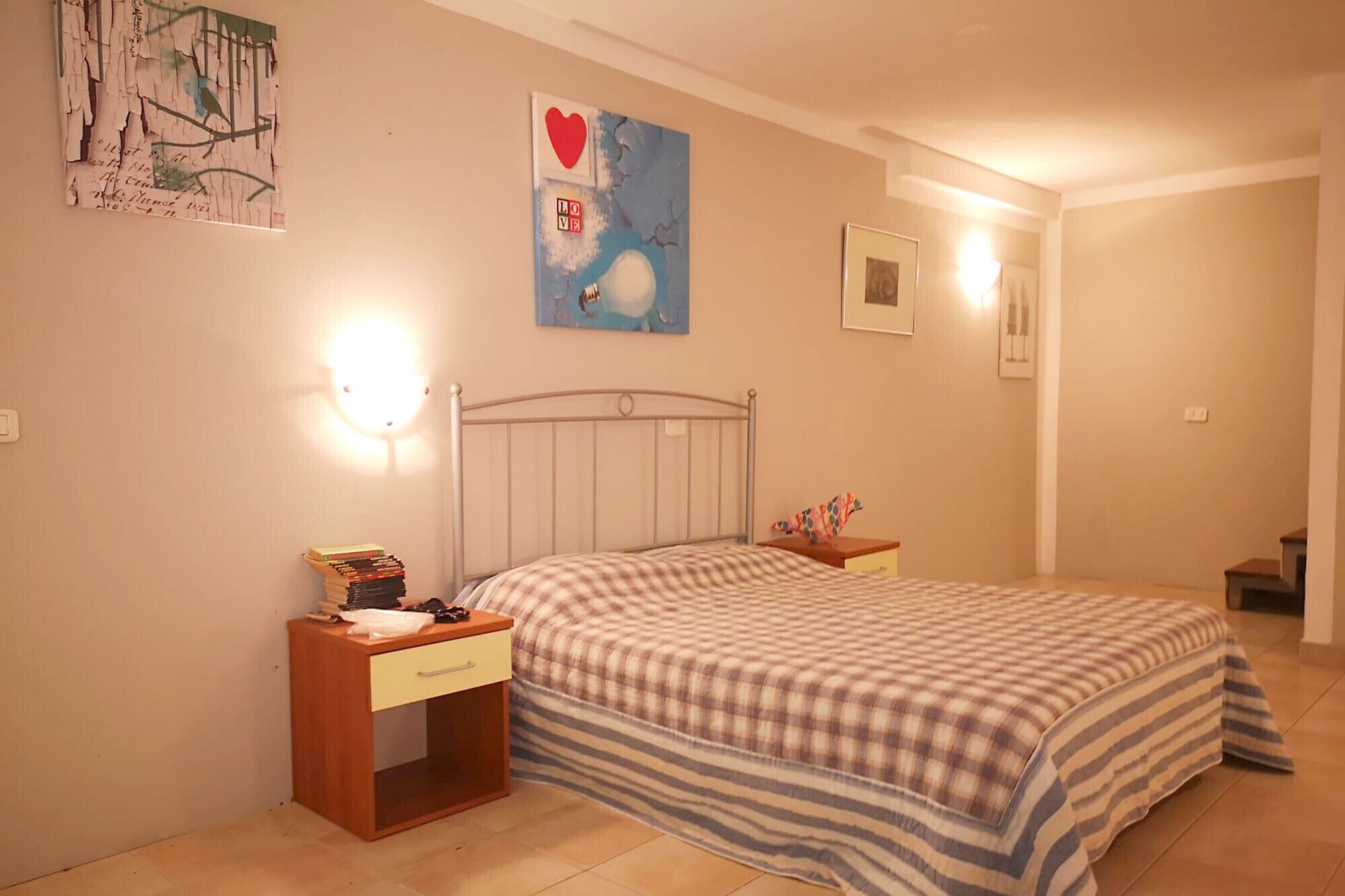 A bedroom with a bed, a nightstand, a wall-mounted light, and a painting.