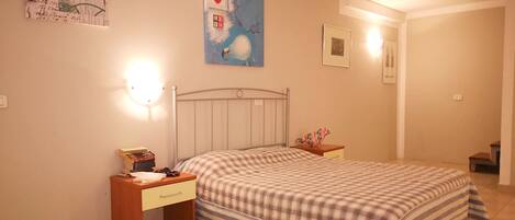 A bedroom with a bed, a nightstand, a wall-mounted light, and a painting.