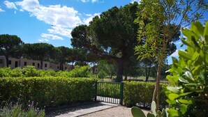 A pathway leading to a building with a green gate, surrounded by lush greenery and trees. - Apartment Bruno at Principina a Mare (Principina a Mare)