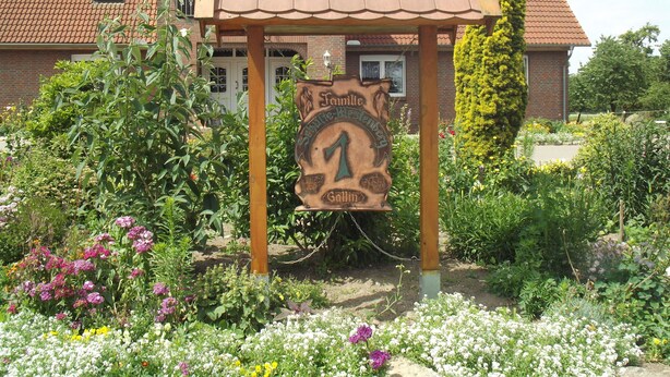 A garden with a wooden sign reading "Familie Restaurant" in front of a house with a tiled roof.