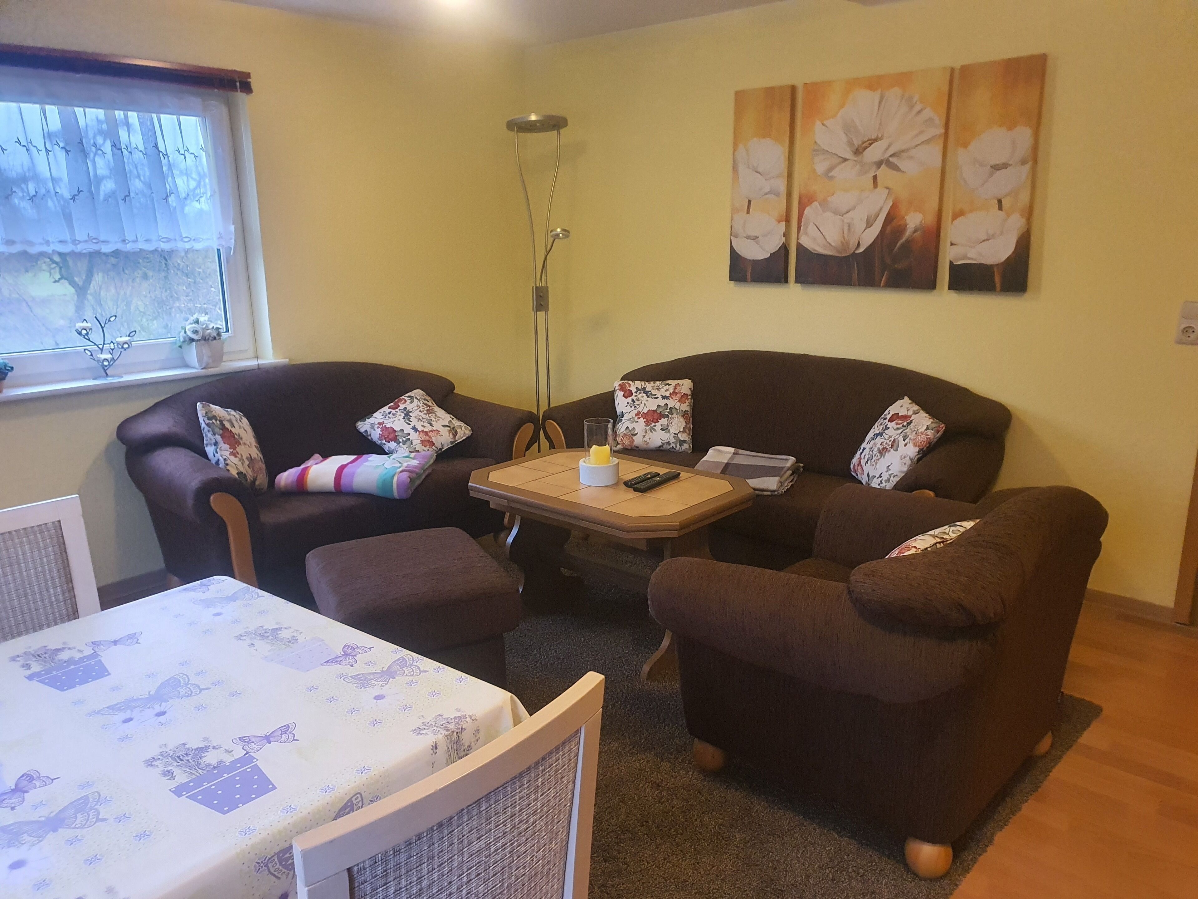 Een gezellige woonkamer met een bruine zithoek, een klein tafeltje en een raam met decoratieve gordijnen.
